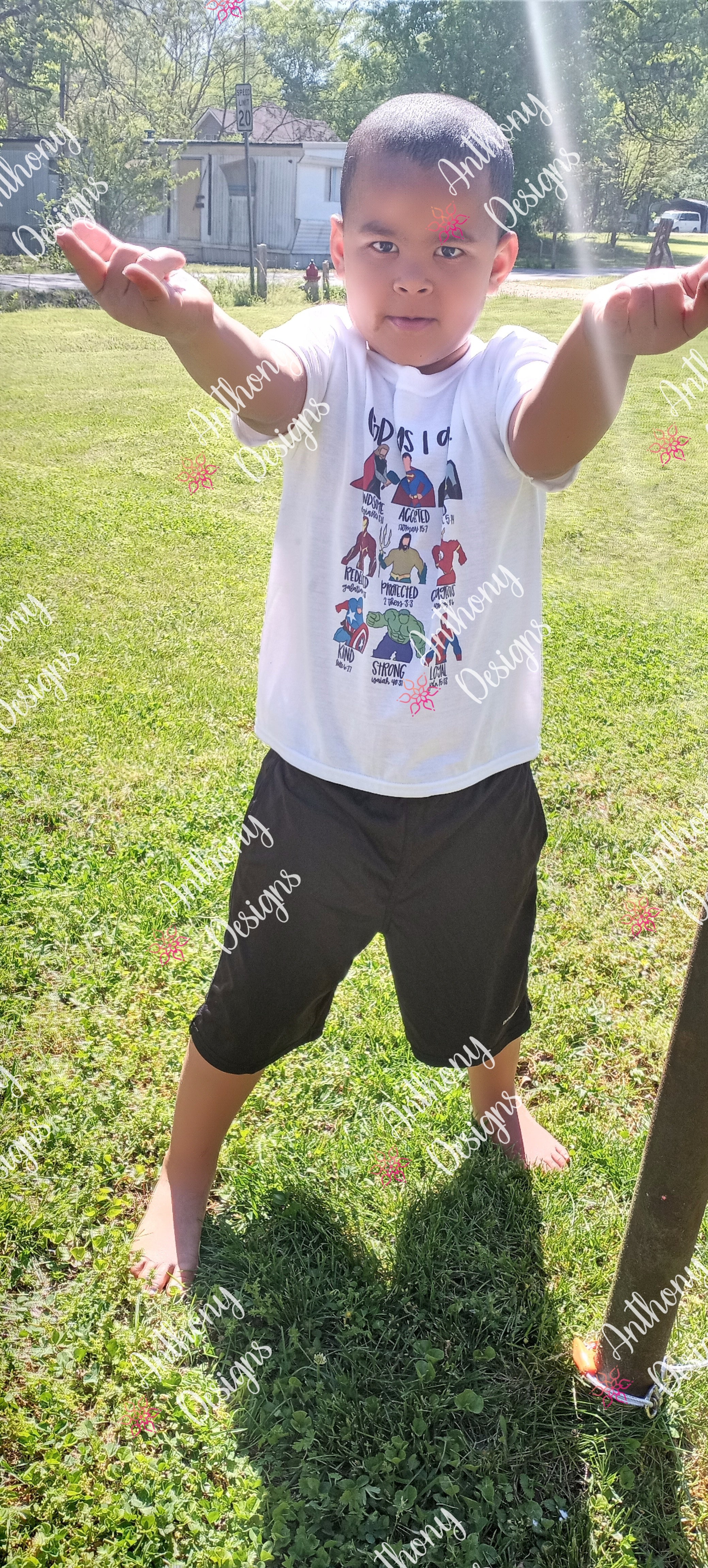 Child standing on grass with arms outstretched, wearing a white t-shirt with graphics and black shorts.